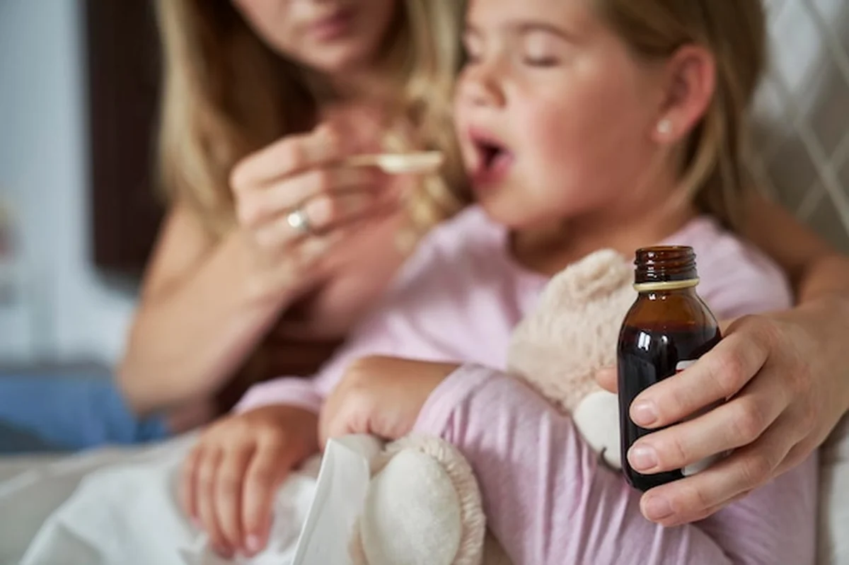 Matka daje syrop chorej dziewczynie w łóżku