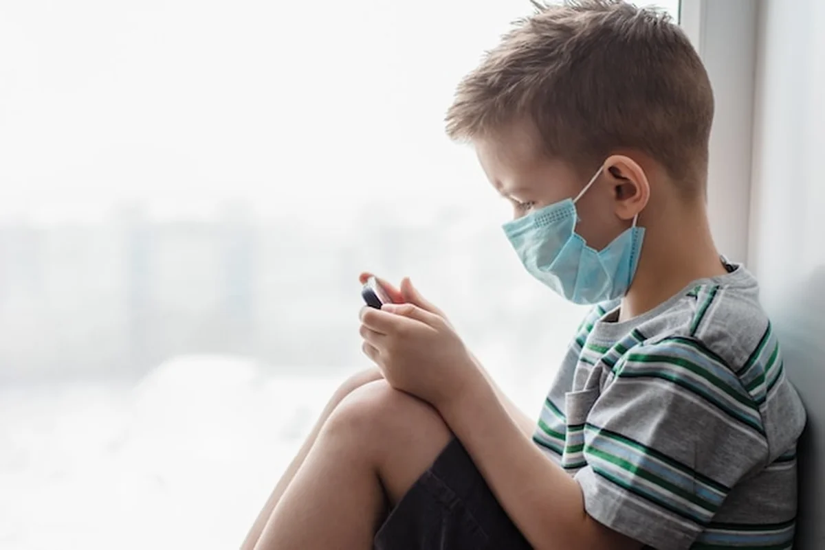 Dziecko w masce medycznej w kwarantannie patrzy na telefon podczas Covid-19